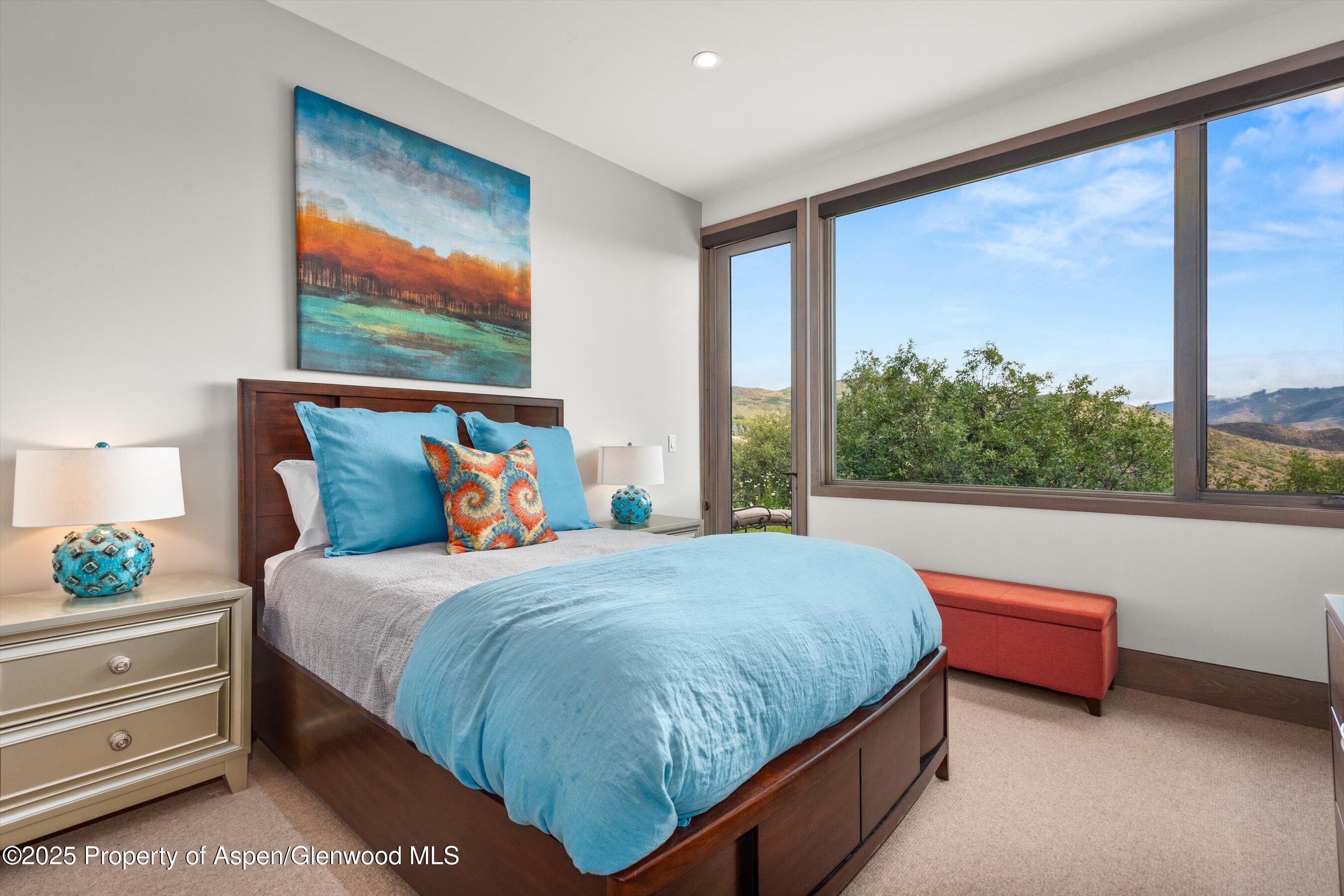 Bedroom with turquoise bedding and large windows overlooking green hills and distant mountains.