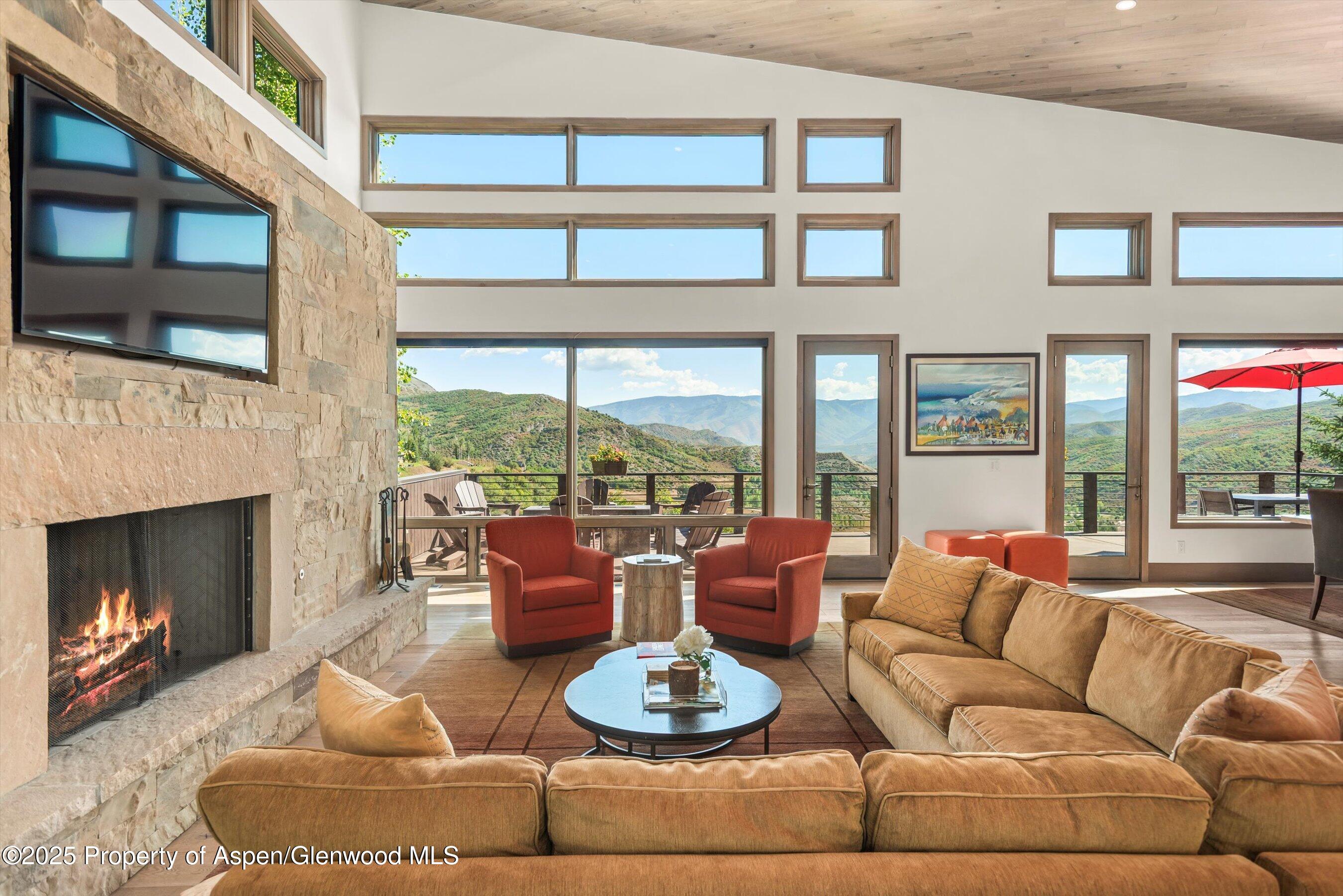 Living room with a stone fireplace, large windows, and mountain views from the deck.