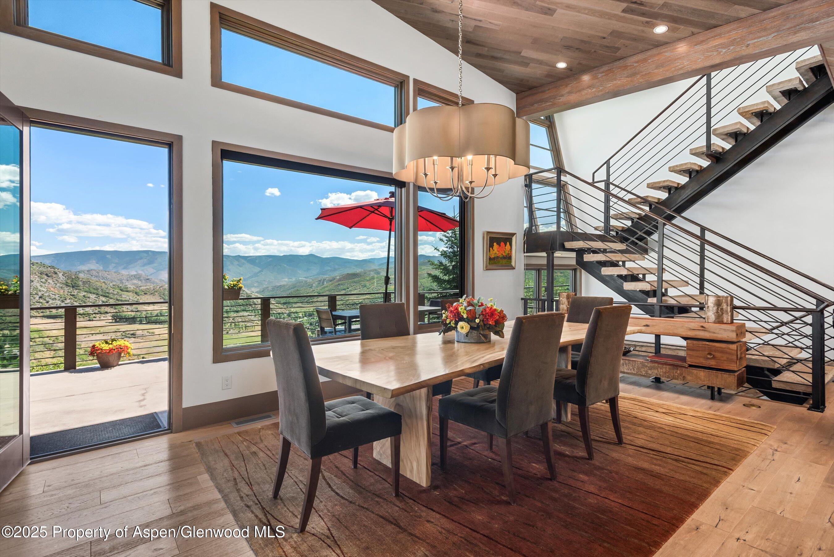 Dining room with a wood table, open staircase, and expansive mountain views through large windows.