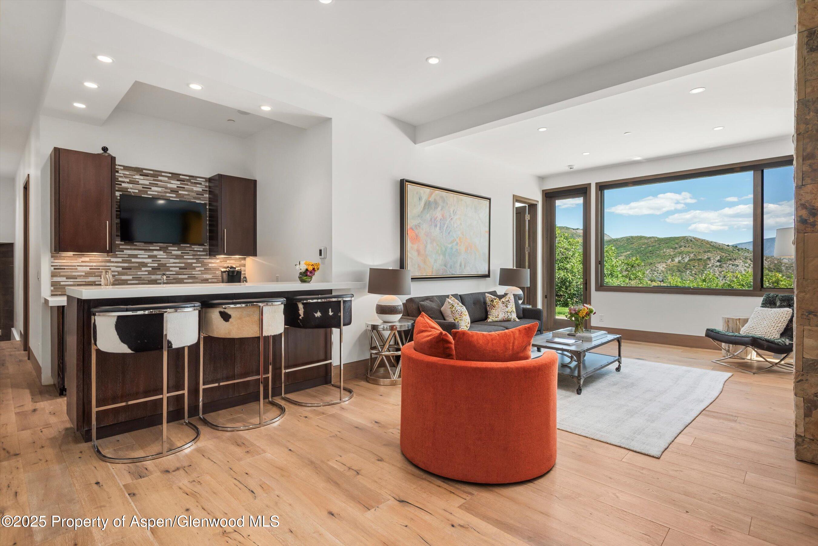 Open-plan living room with an orange chair, bar seating, and mountain views through large windows.