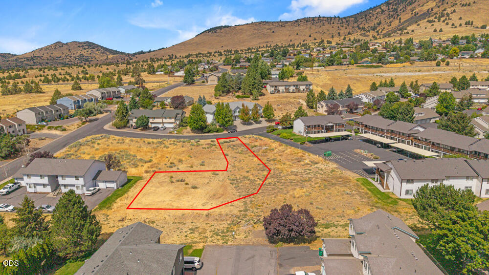 Vacant lot outlined in red among homes, with rolling hills behind it.