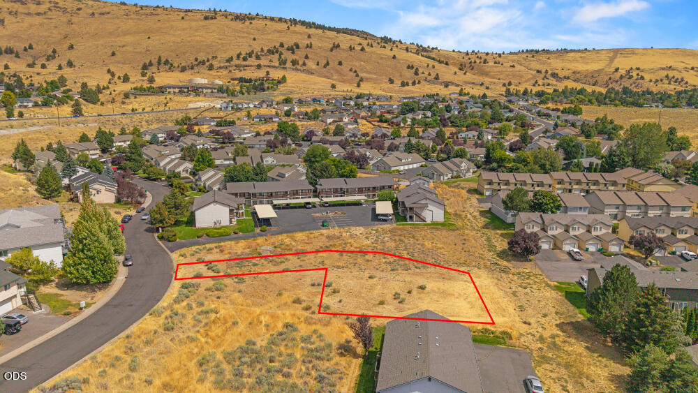 Vacant lot outlined in red beside a residential neighborhood, with rolling hills beyond.