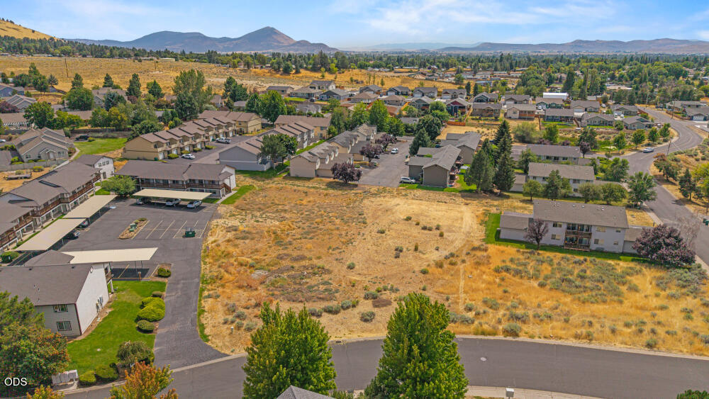 Aerial view of an undeveloped parcel among neighborhood buildings, with mountains in the distance.