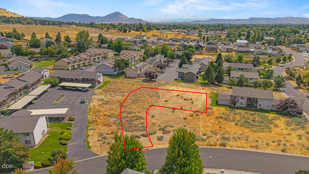 Vacant lot outlined in red among apartment buildings and homes, with distant hills.