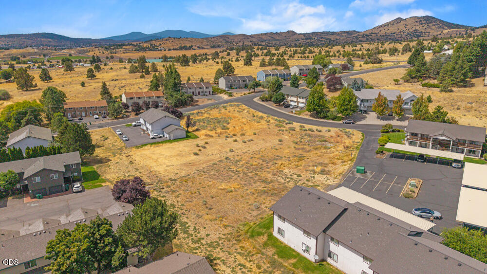 Aerial view of a dry vacant lot among homes, with hills and mountains beyond.