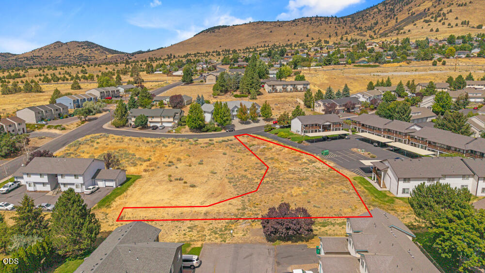 Aerial view of a vacant lot outlined in red among buildings beneath dry hills.