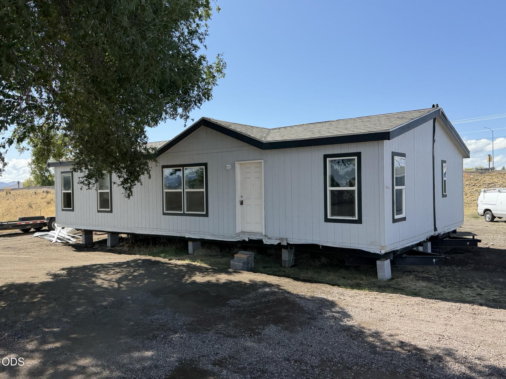 Light gray manufactured home elevated on blocks, with dark-trimmed windows and a white front door.