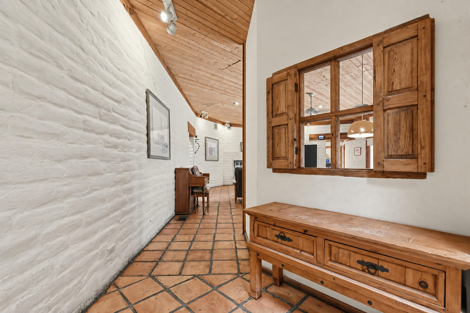 Hallway with white brick walls, terracotta tile, wood ceiling, and a shuttered interior window.