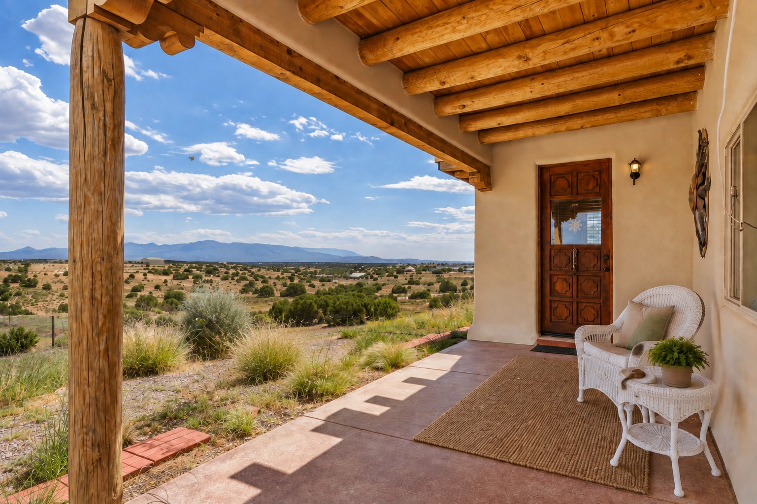 Covered porch with timber beams and wicker seating overlooking open scrubland and distant mountains.