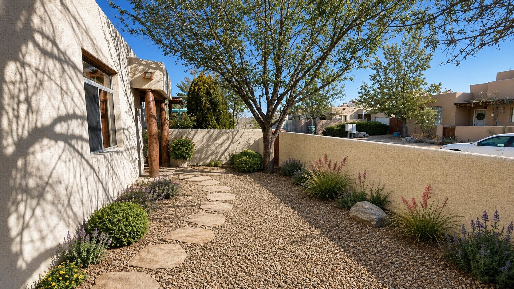 Landscaped courtyard with a stepping-stone path, flowering plants, and a mature shade tree beside a stucco home.