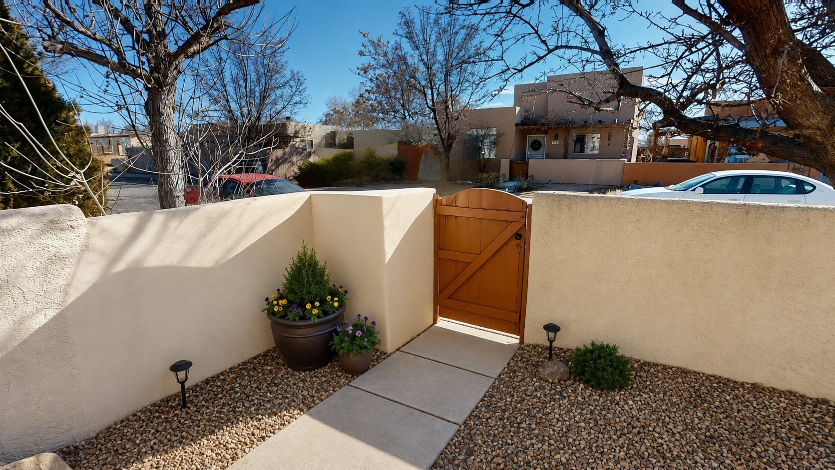 Front entry courtyard with a wooden gate, stucco walls, stone path, and potted flowers.