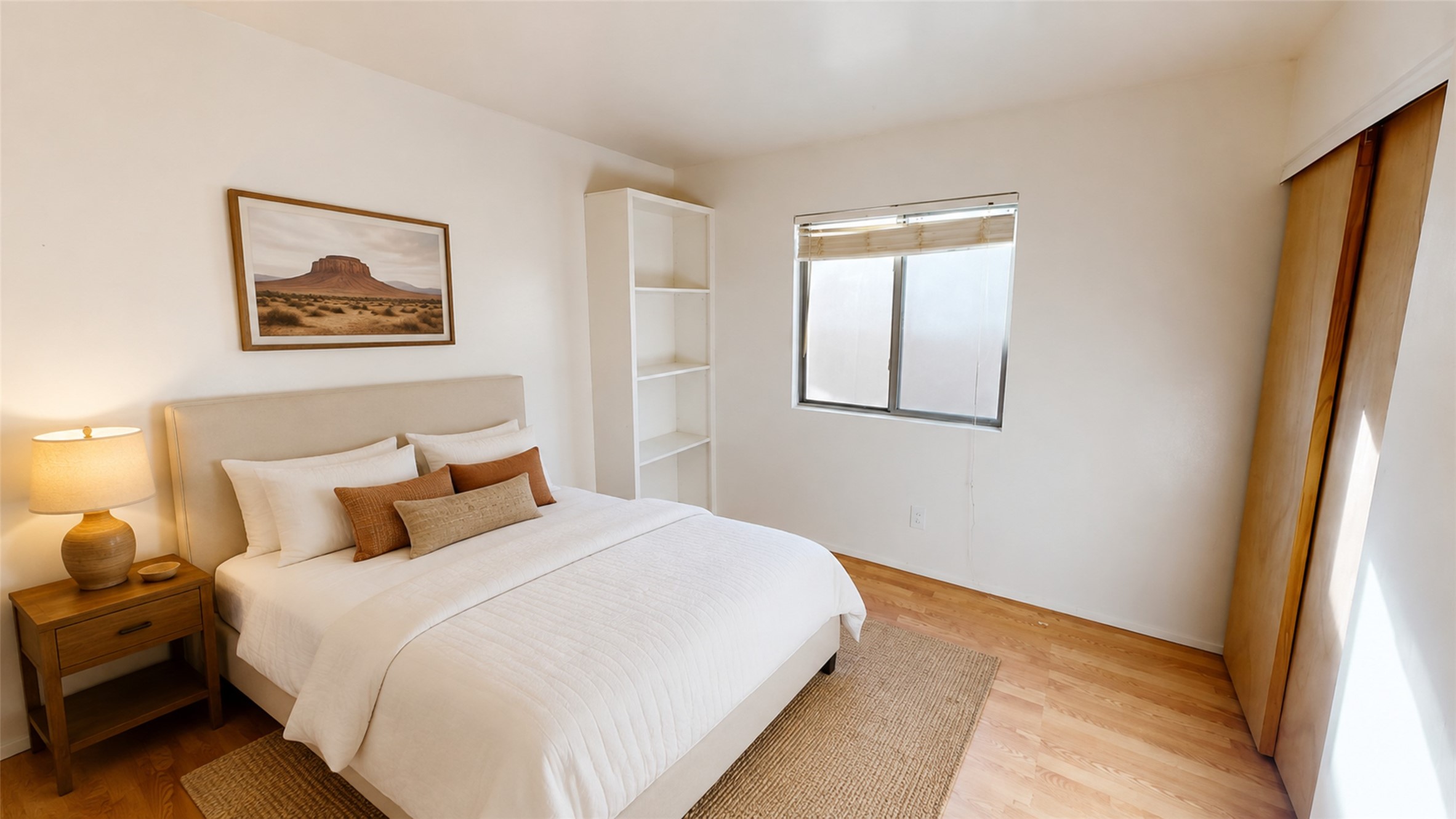 Bedroom with a white bed, brown accent pillows, built-in shelving, and warm wood floors.