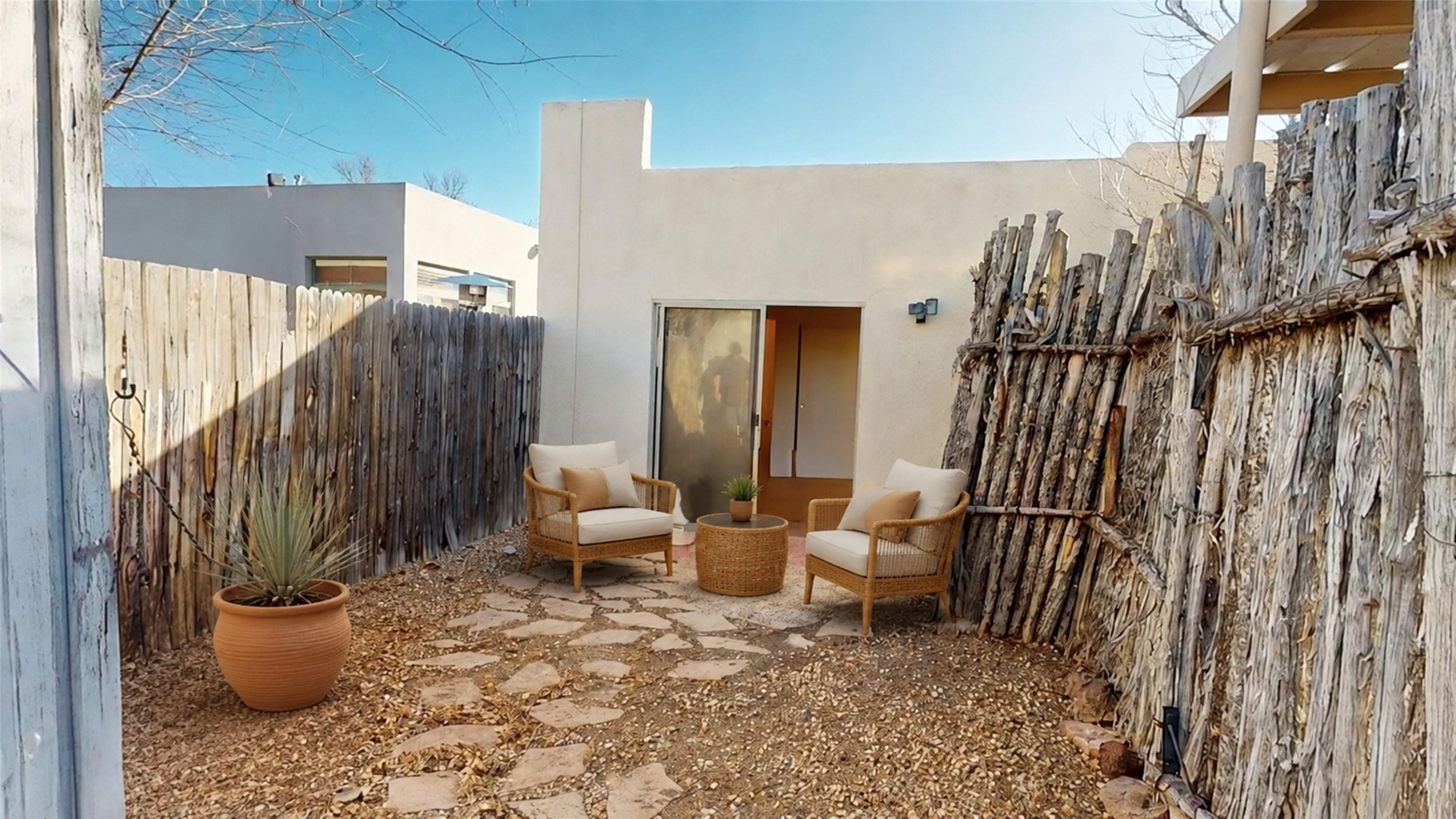 Furnished courtyard with wicker chairs, flagstone path, potted yucca, and rustic branch fencing.