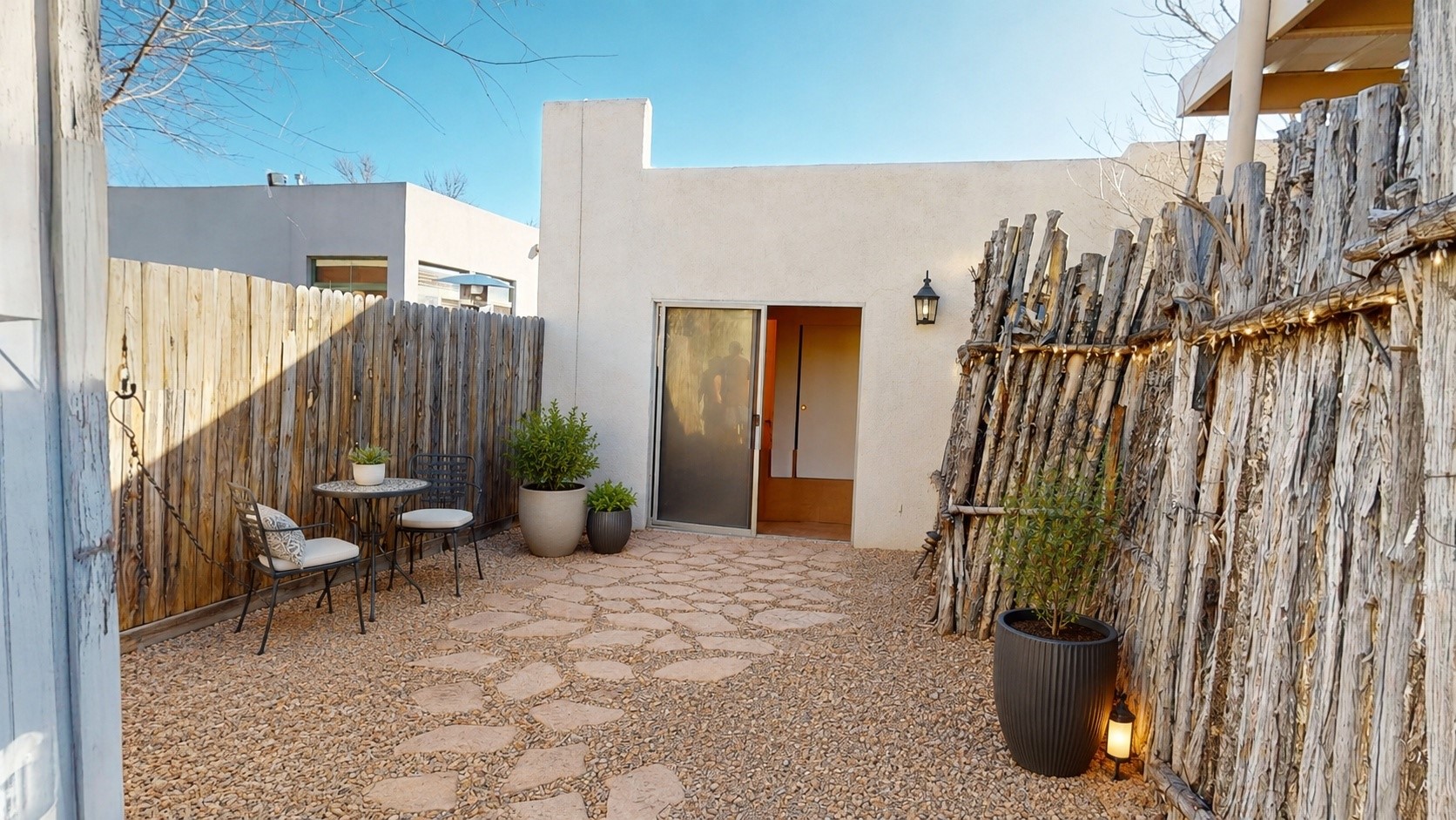 Private courtyard with rustic wood fencing, stone pavers, patio seating, and potted plants.