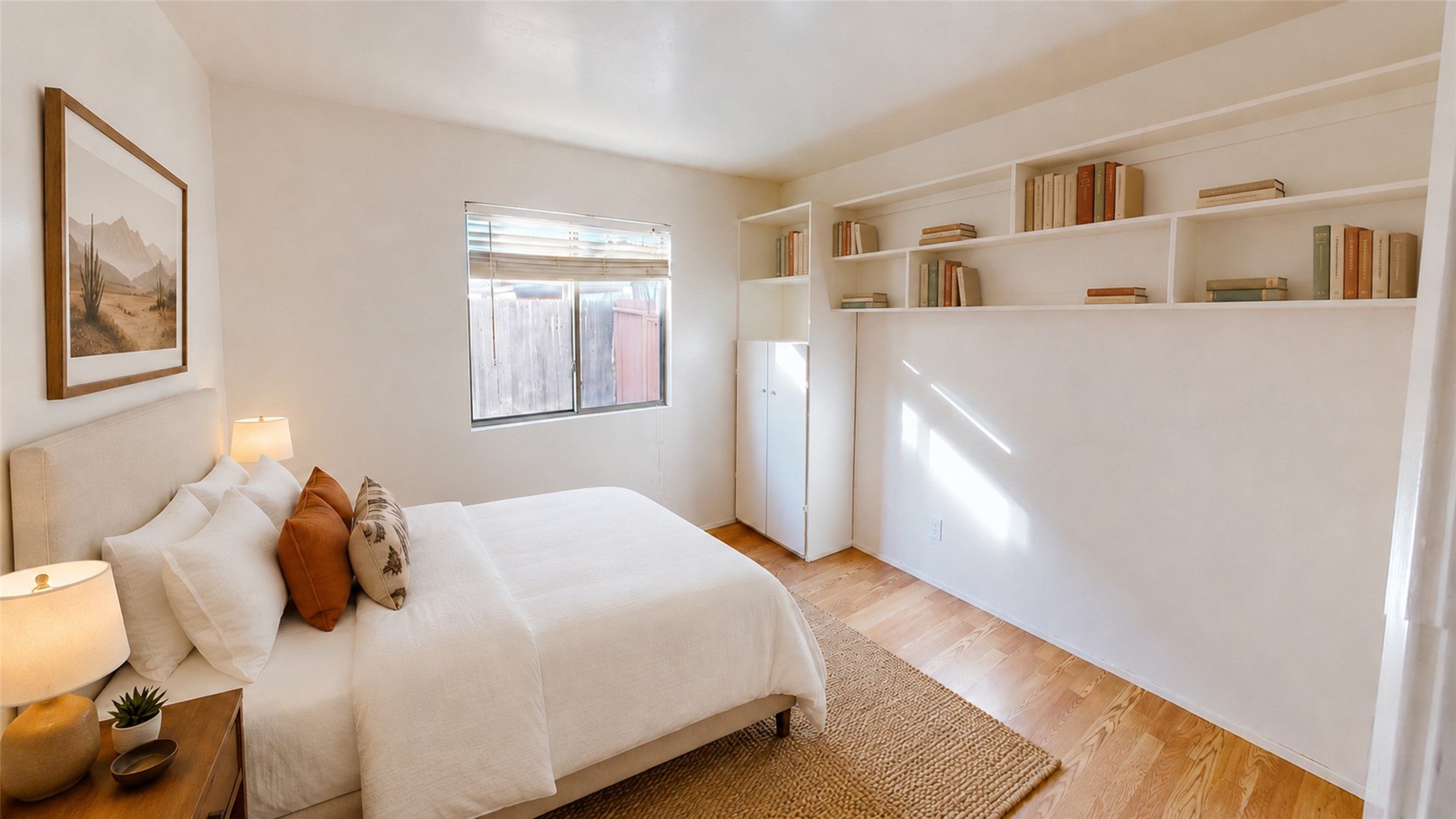 Staged bedroom with a white bed, built-in bookshelves, and light wood flooring.