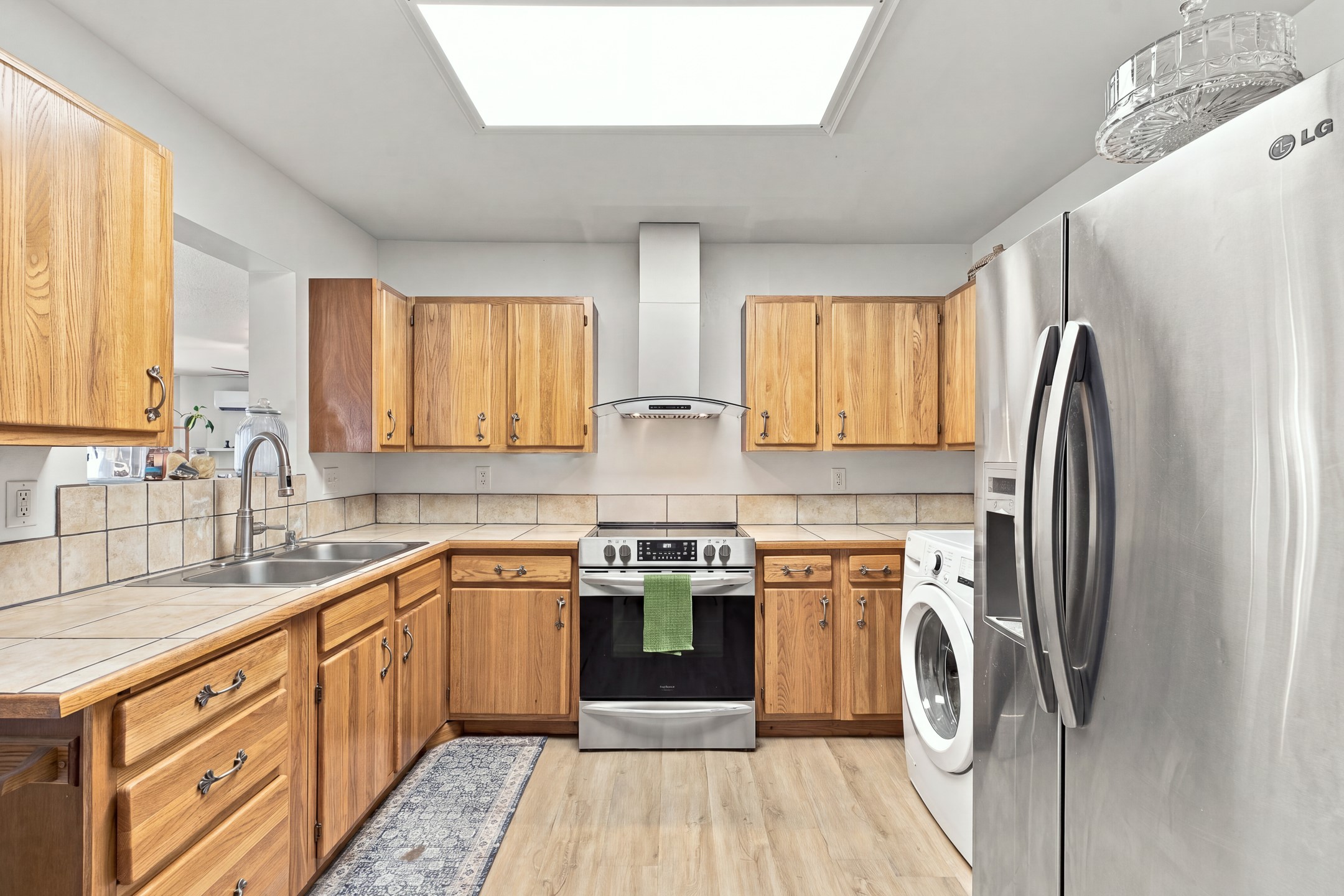 Kitchen with wood cabinets, tiled counters, stainless appliances, and a washer beside the refrigerator.