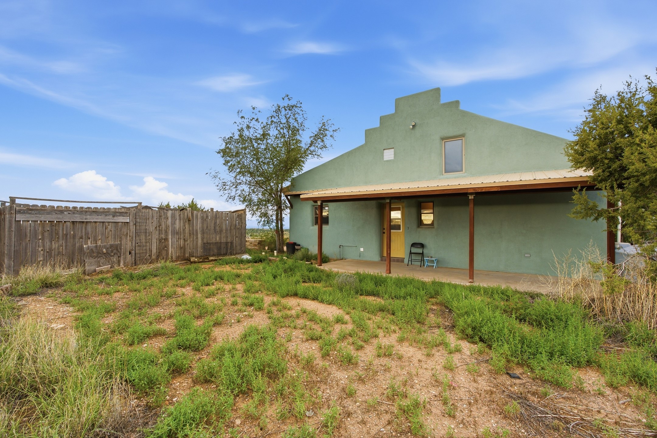 Green stucco home with a covered porch, stepped parapet roof, and fenced yard.