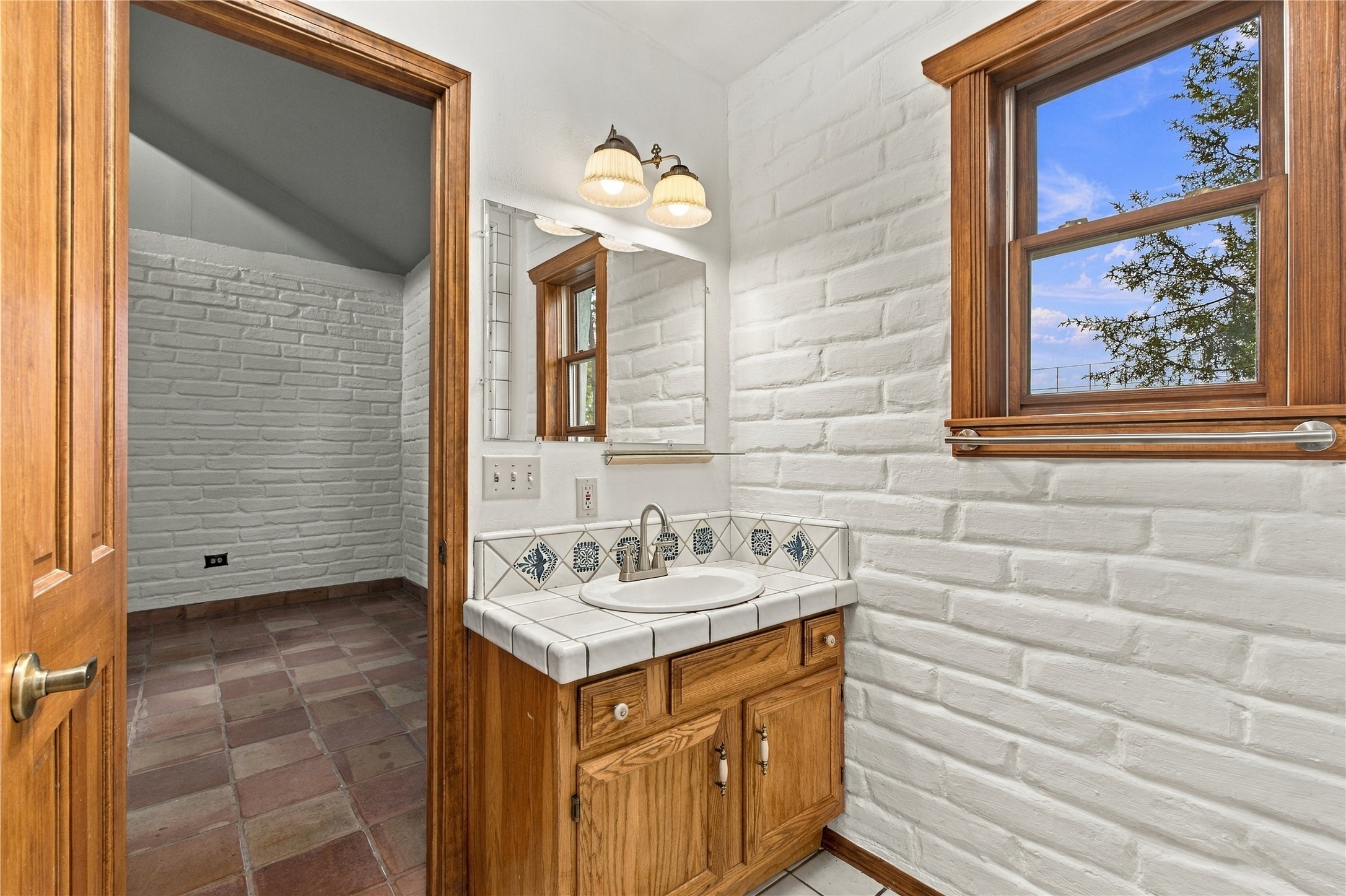 Bathroom with a tiled vanity, white brick walls, and a wood-trimmed window.