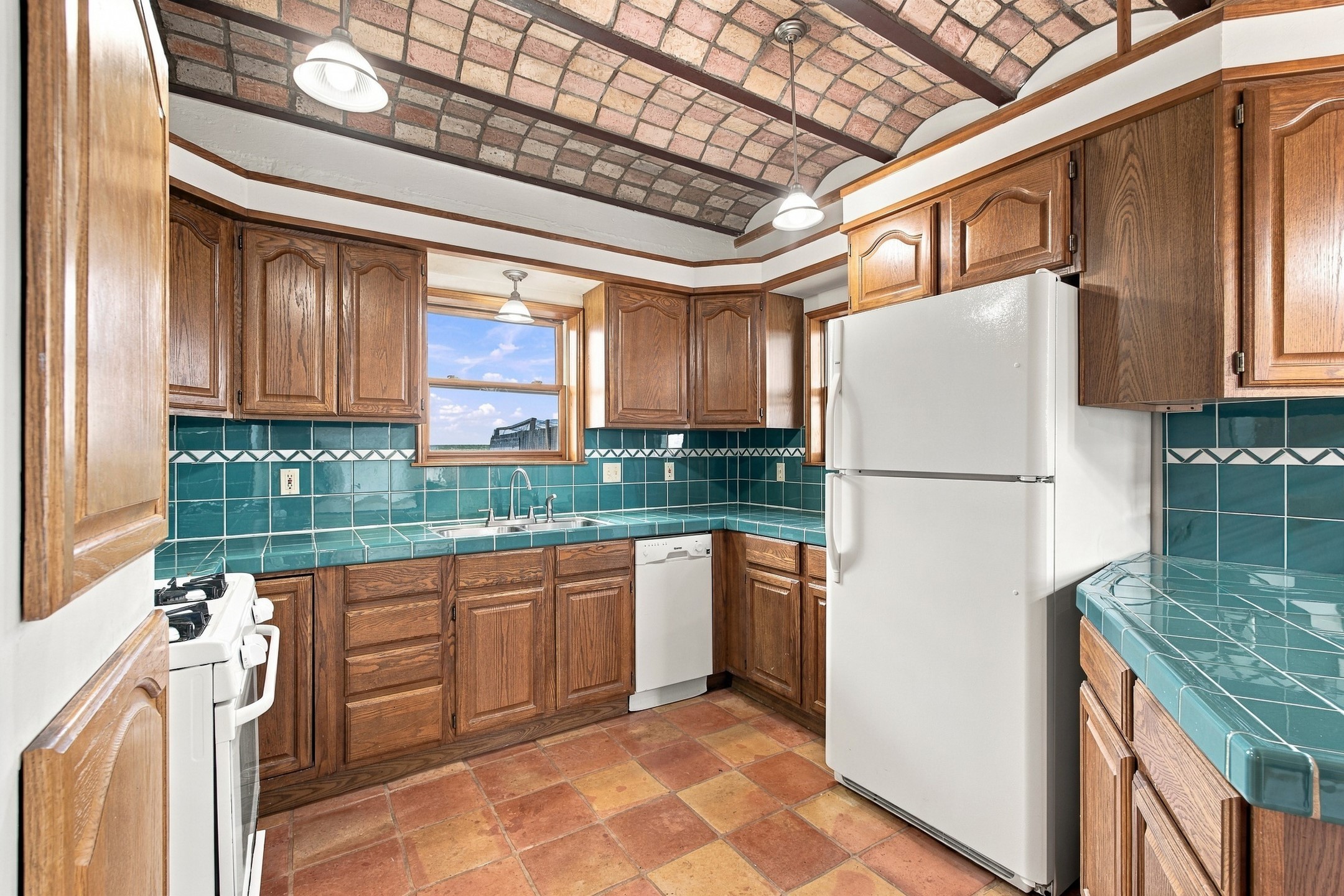 Kitchen with turquoise tile counters, dark wood cabinets, and a vaulted brick ceiling.