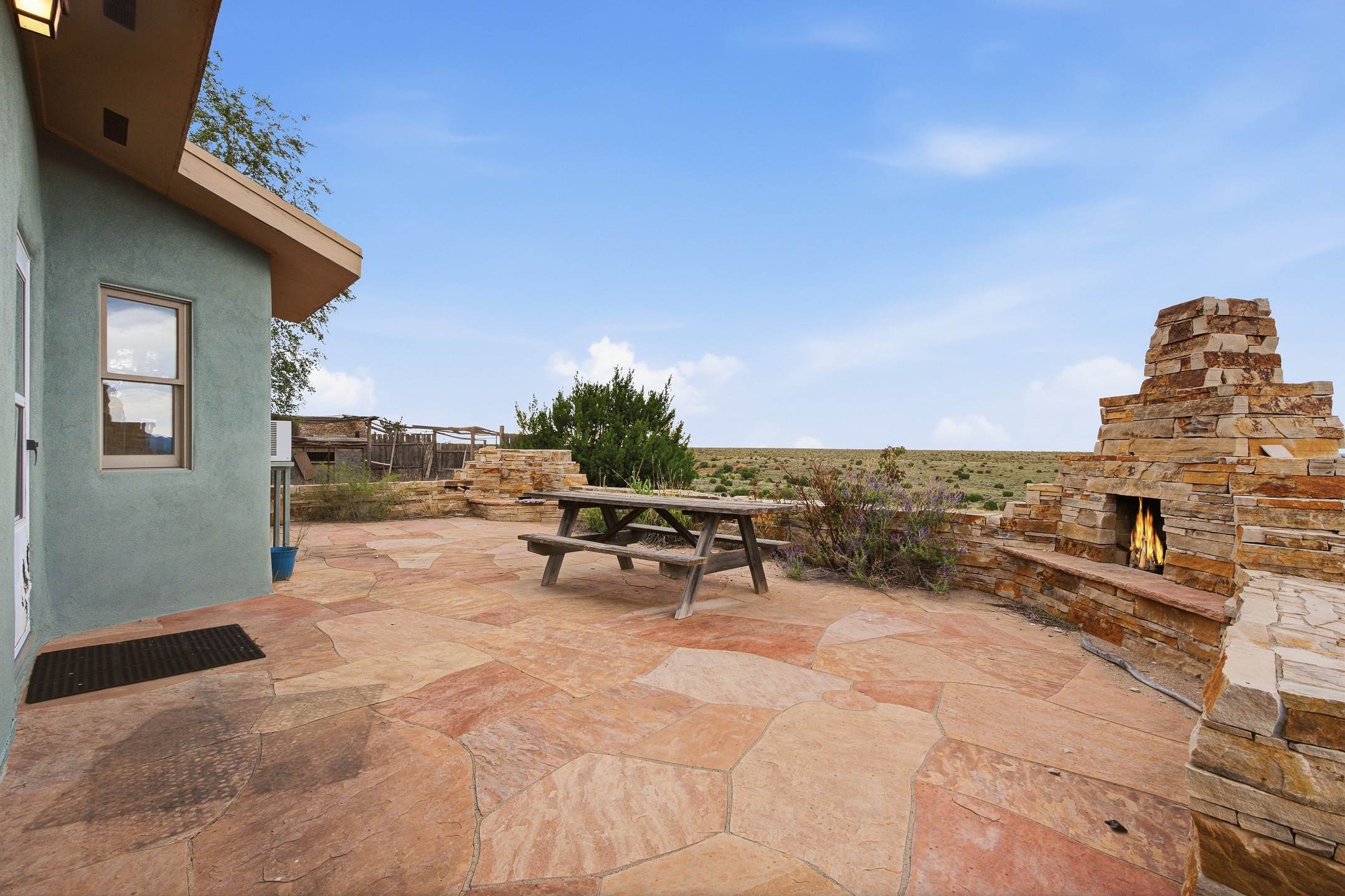 Flagstone patio with a picnic table and stone fireplace overlooking open scrubland.