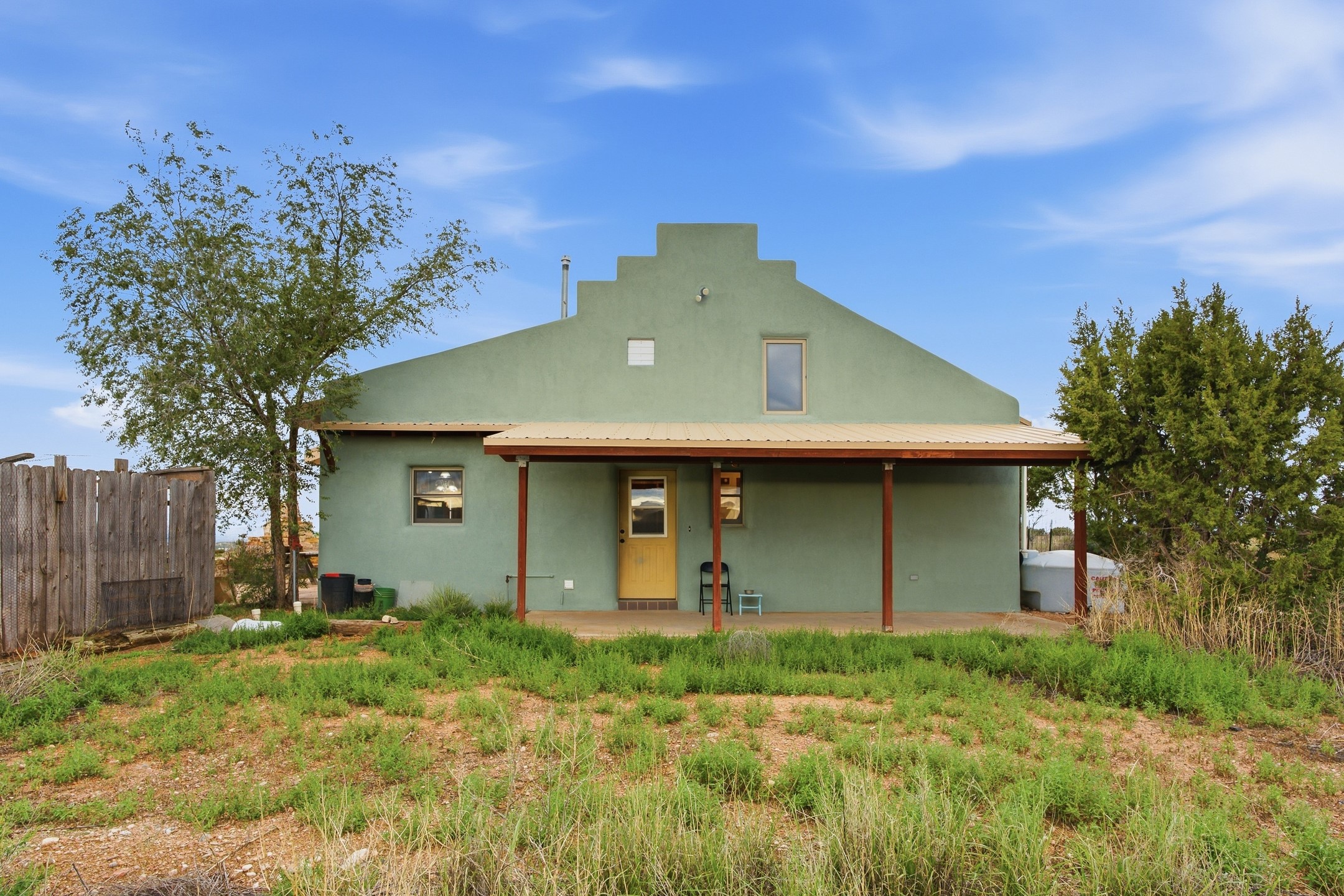 Sage-green house with a stepped roofline, covered porch, and yellow front door.