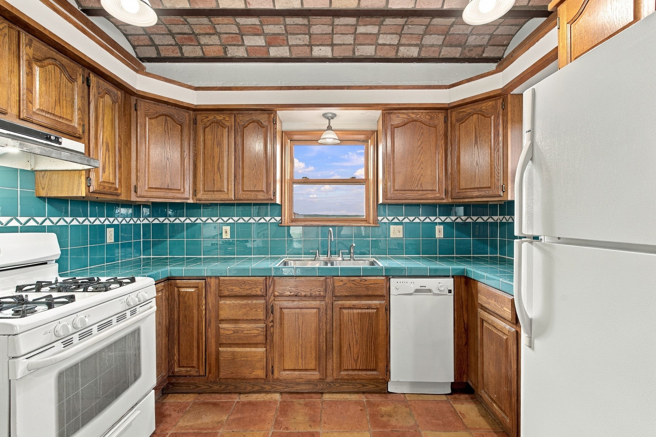 Kitchen with turquoise tile, wood cabinets, and a window above the sink.
