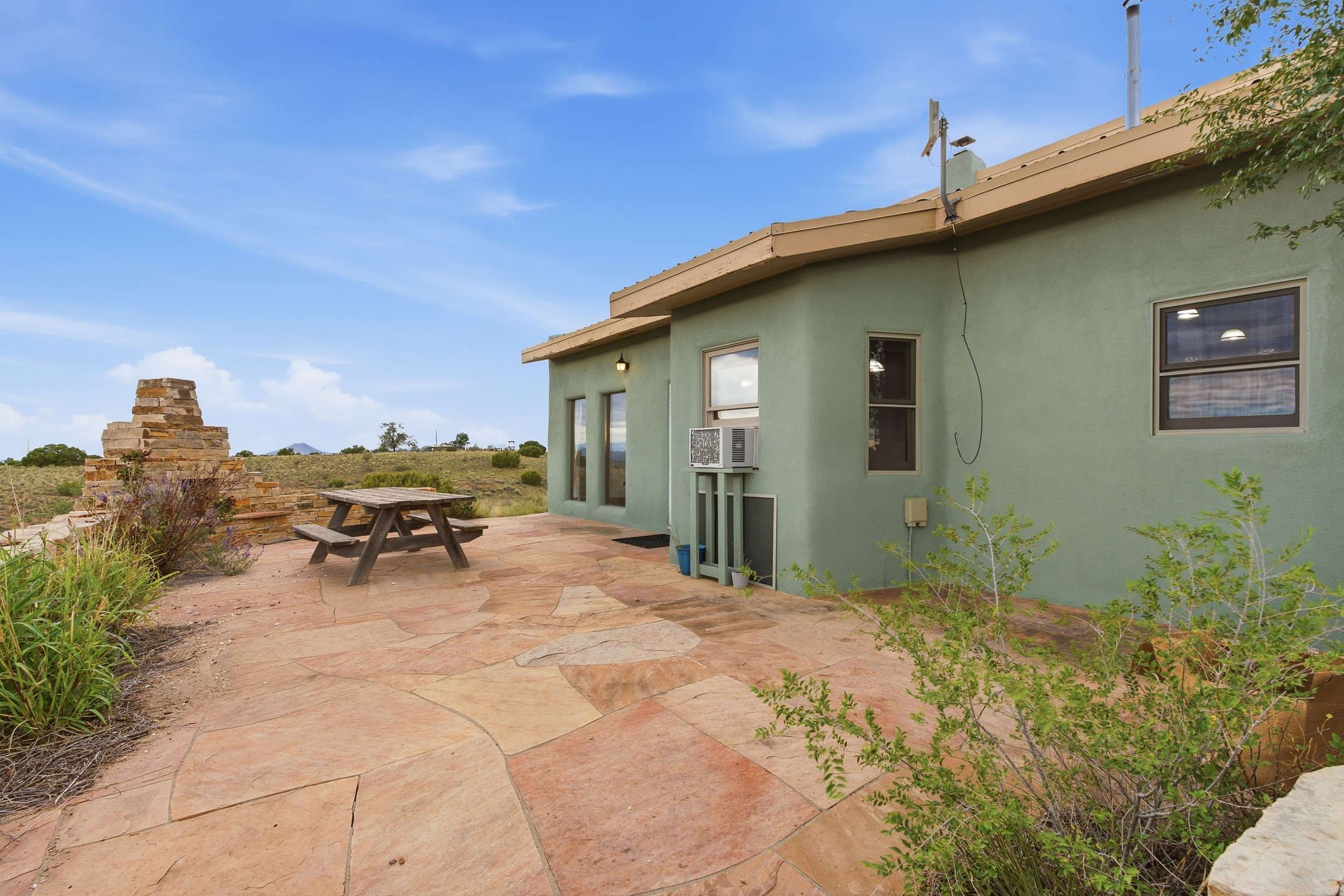 Stone-paved patio beside a green stucco home, with a picnic table and distant hills.