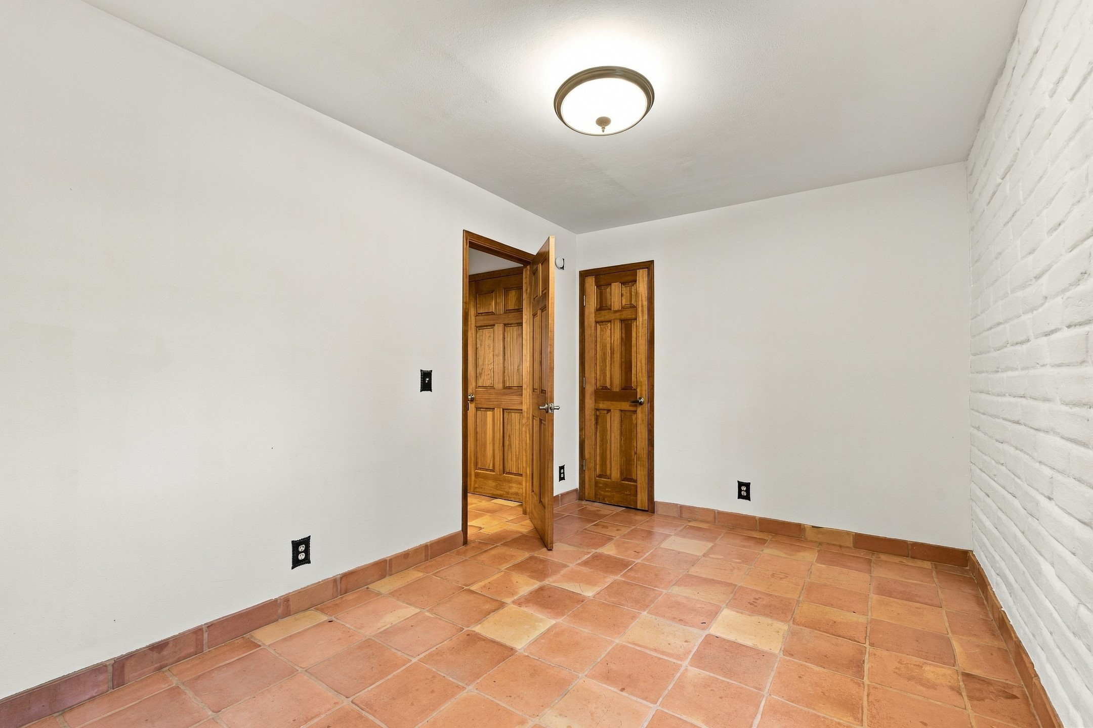 Empty room with terracotta tile floors, a white brick wall, and wooden doors.