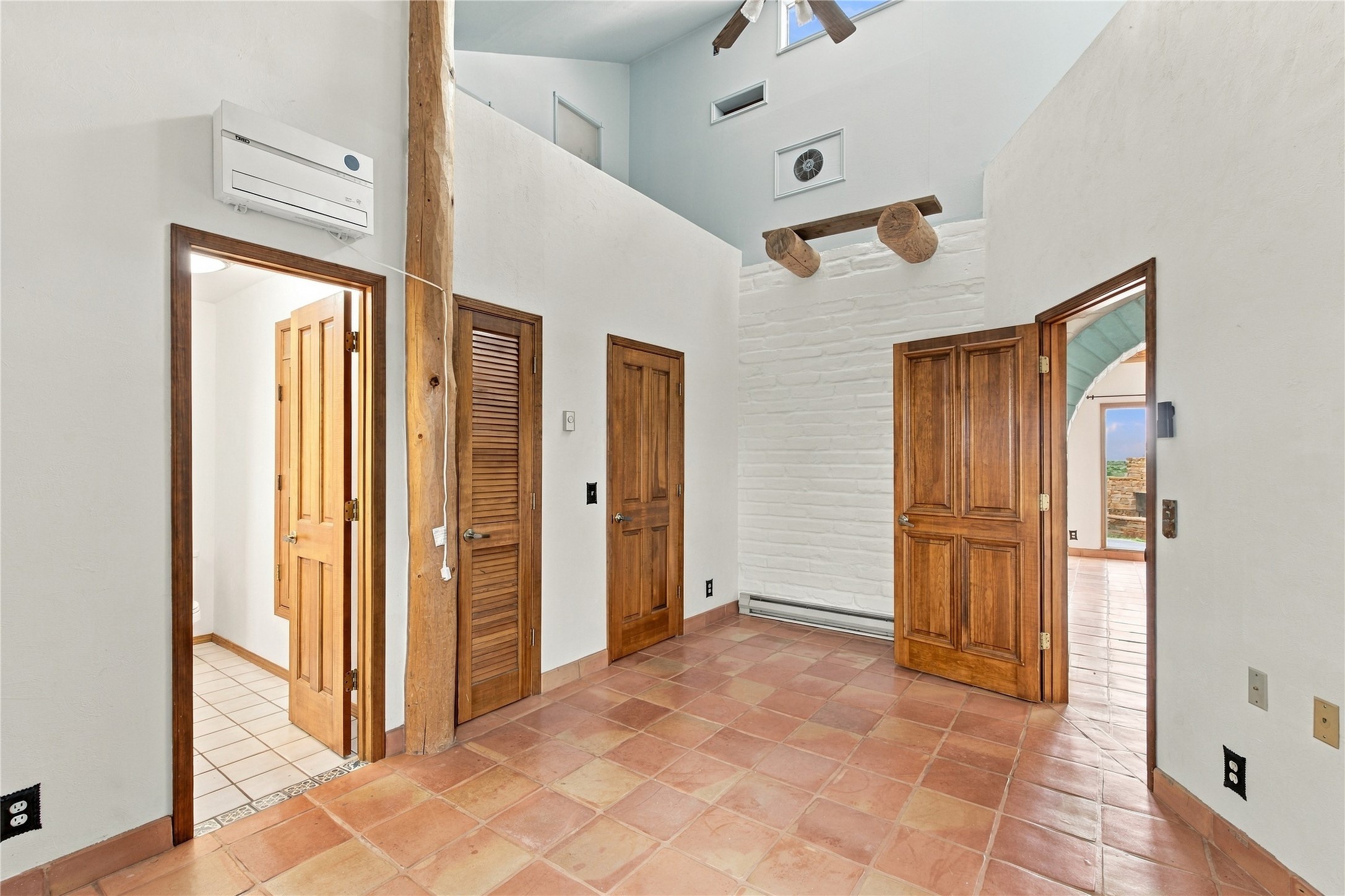 Foyer with terracotta tile, exposed wooden beams, and several wood doors.