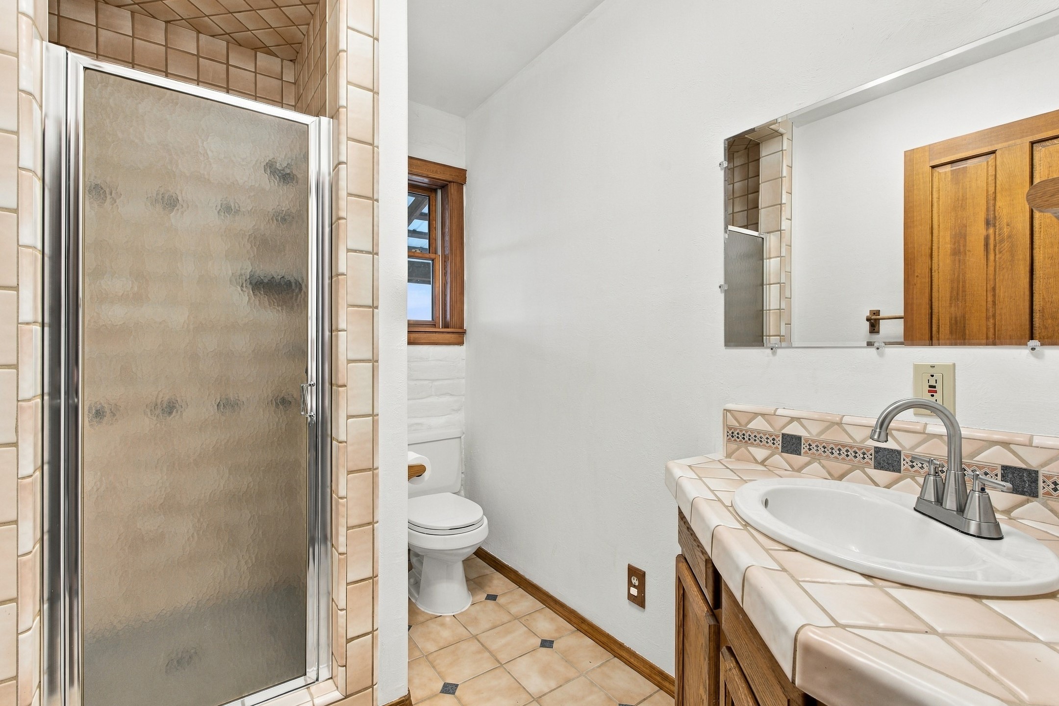 Bathroom with a frosted-glass tiled shower and a tiled vanity with an oval sink.