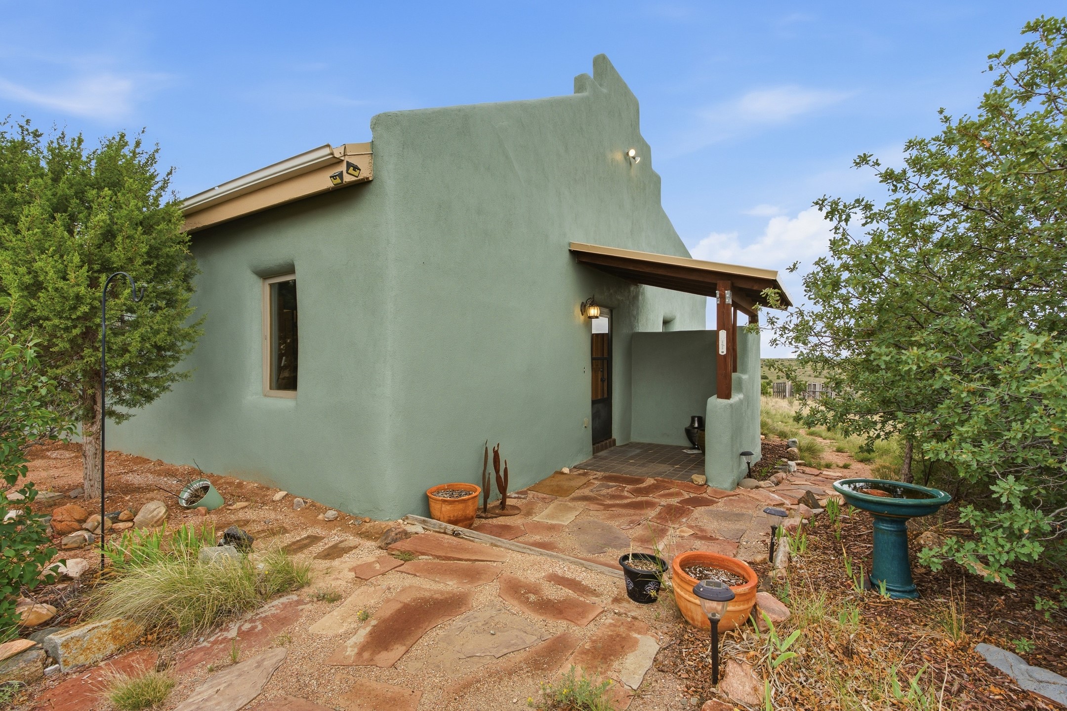 Green Southwestern-style home with a covered entry, stone patio, and potted plants.