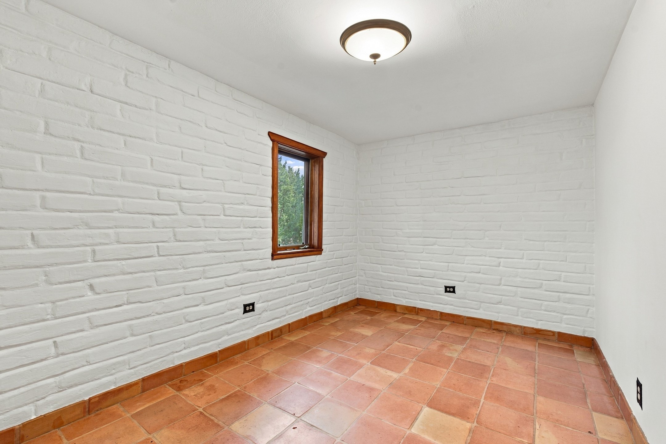 Empty room with white brick walls, terracotta tile flooring, and a narrow wood-trimmed window.