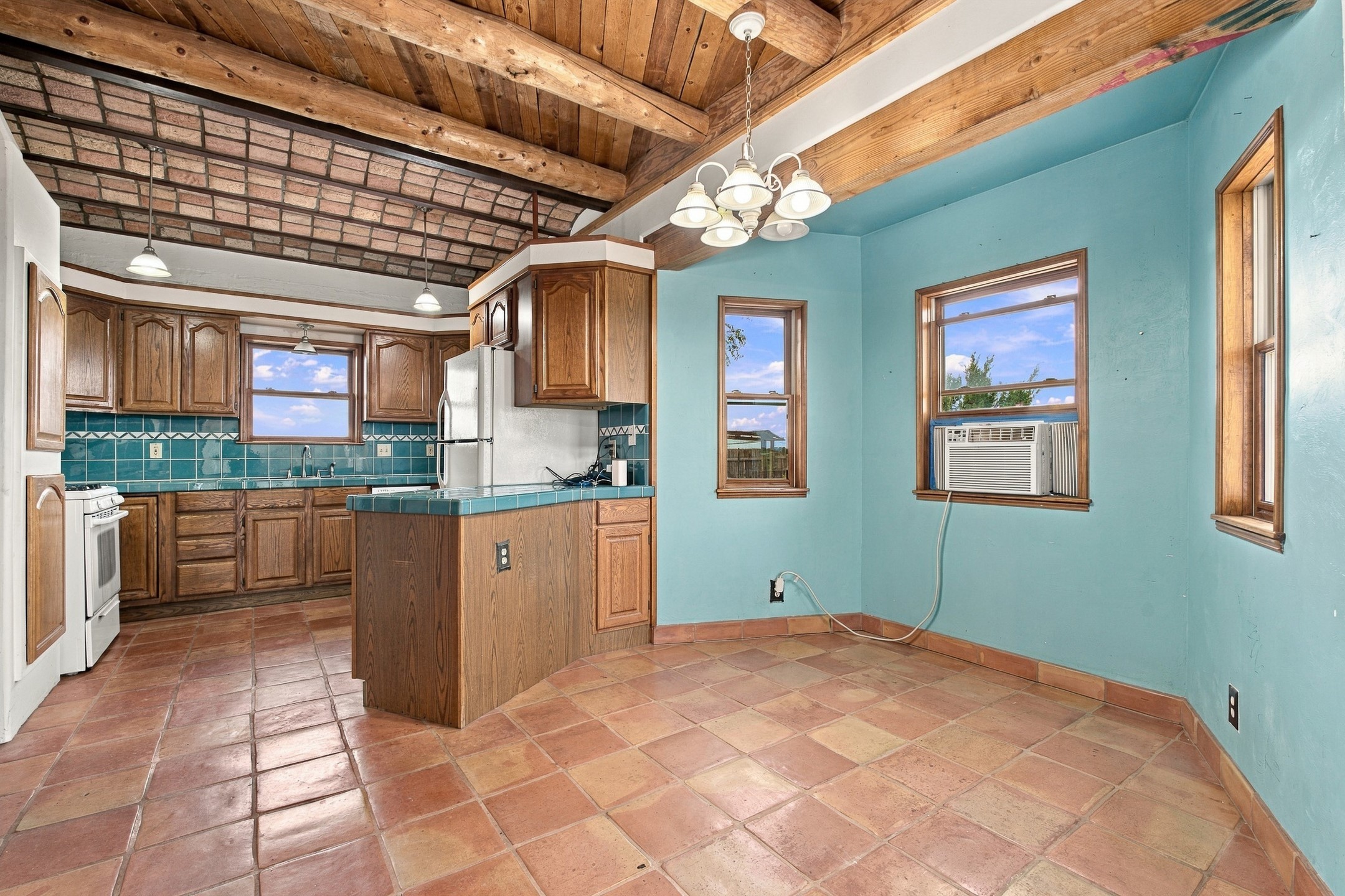 Kitchen with wood cabinets, turquoise tile backsplash, terracotta floors, and a vaulted wood ceiling.