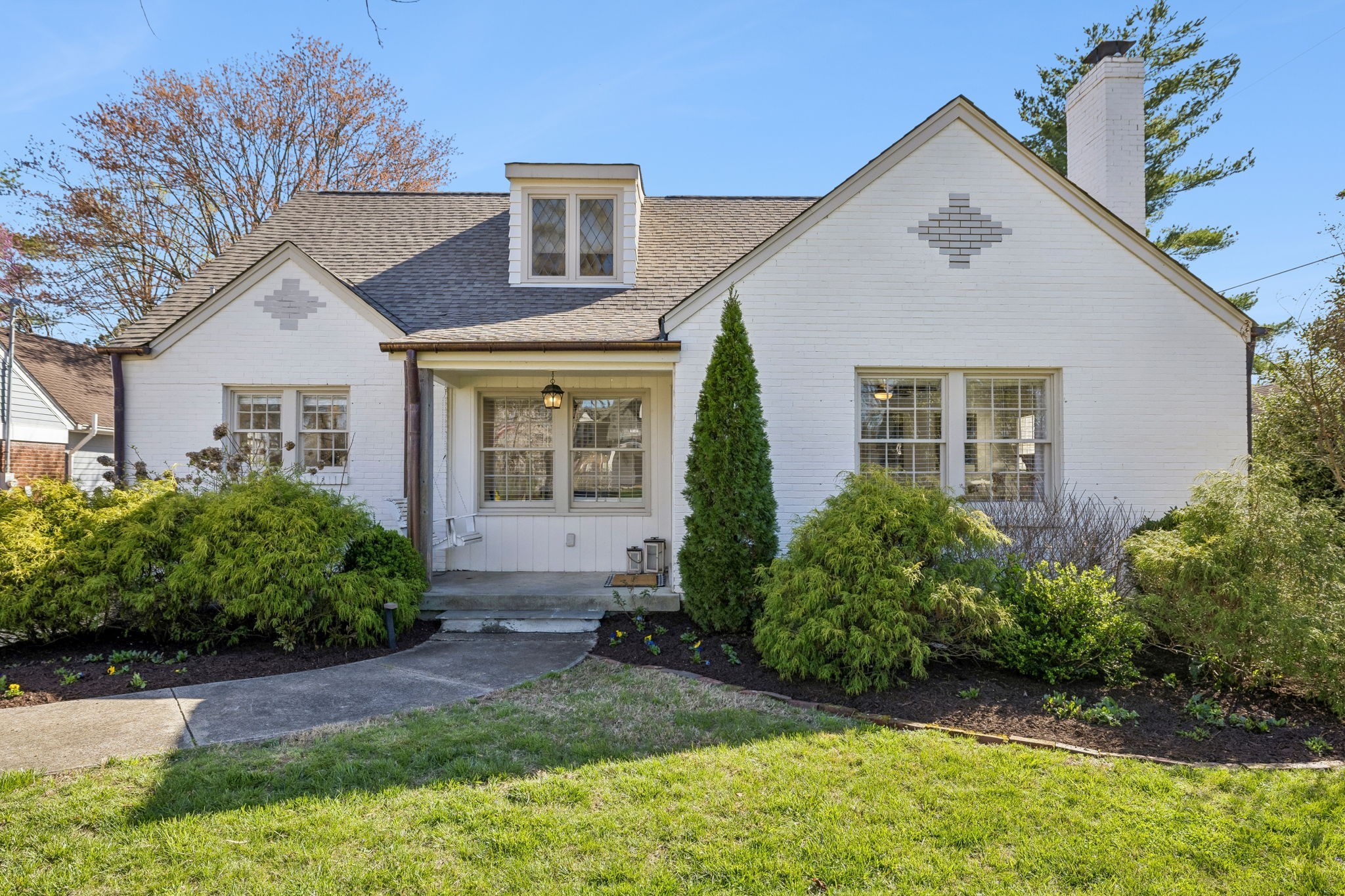 White brick home with a steep gabled roof, covered entry, and landscaped front yard.