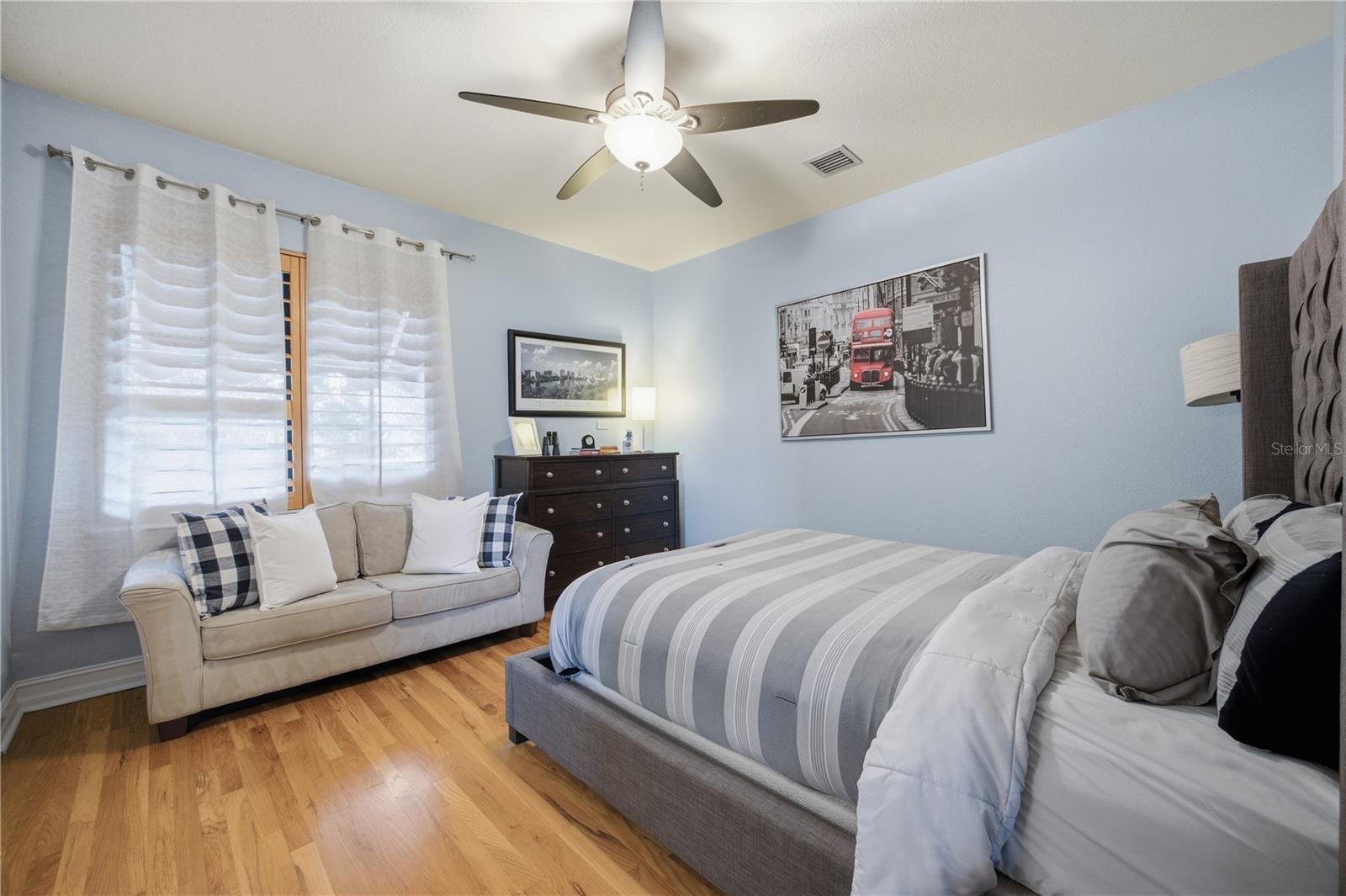Bedroom with a striped bed, cream sofa, hardwood floors, and pale blue walls.