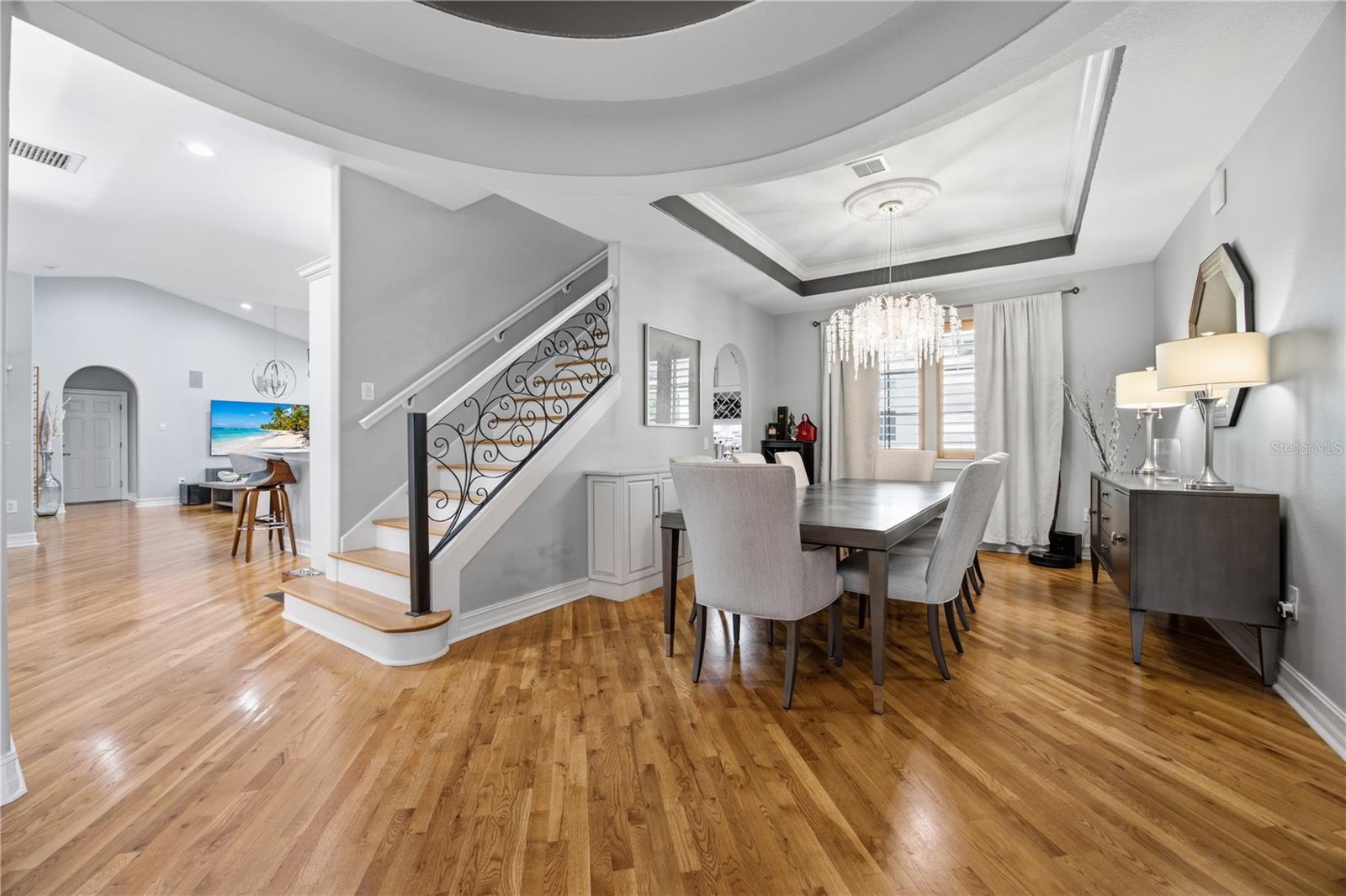 Dining room with a crystal chandelier, hardwood floors, and a decorative staircase.
