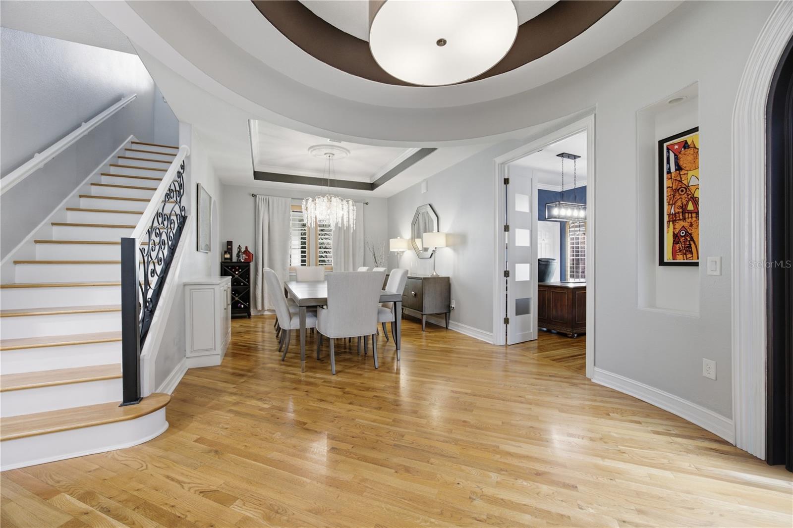 Dining room and entry with a hardwood floor, ornate staircase railing, chandelier, and circular tray ceiling.