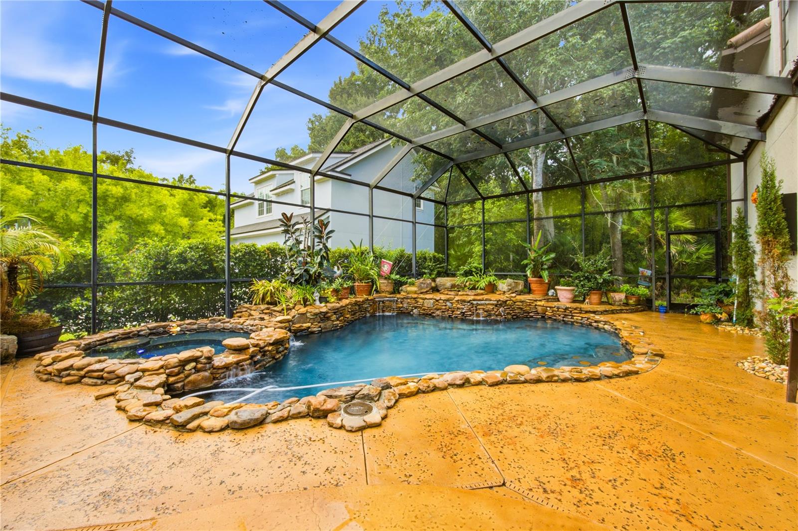 Swimming pool with natural stone edging and potted plants beneath a screened enclosure.