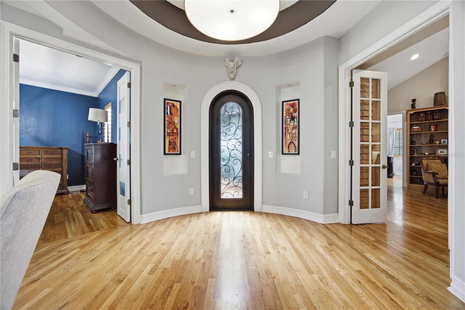 Foyer with an arched glass front door, light hardwood floors, and open doorways to adjoining rooms.