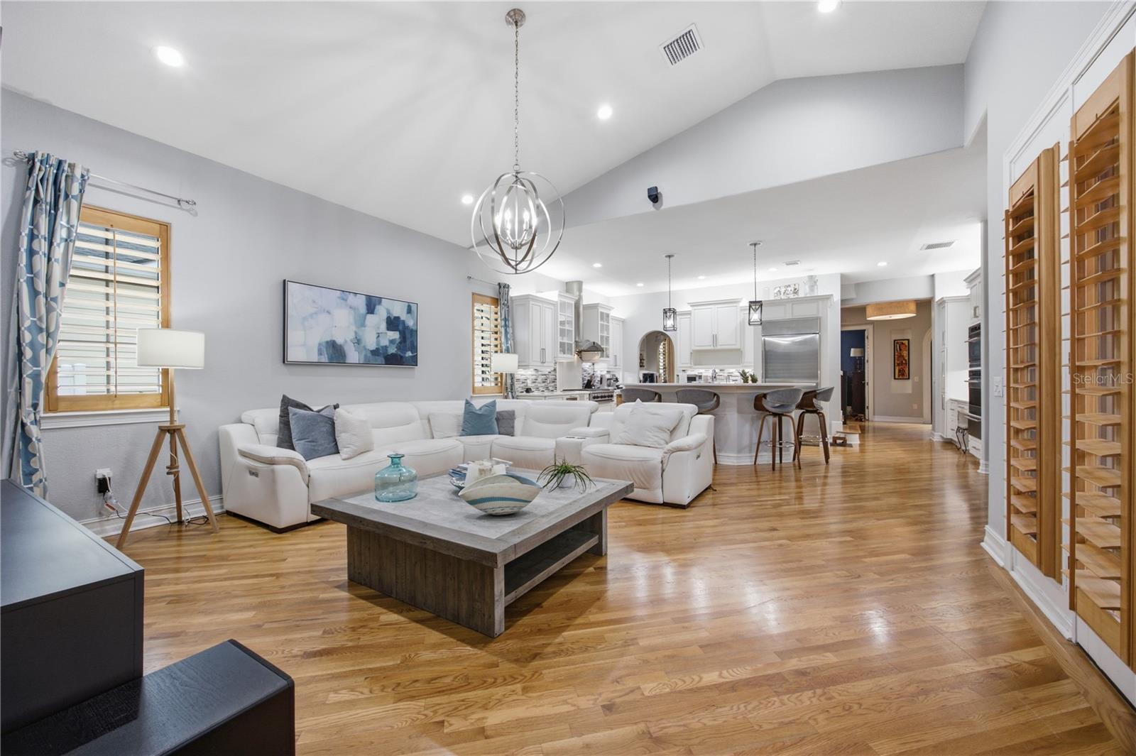 Open-plan living room and kitchen with a white sectional, hardwood floors, and a vaulted ceiling.