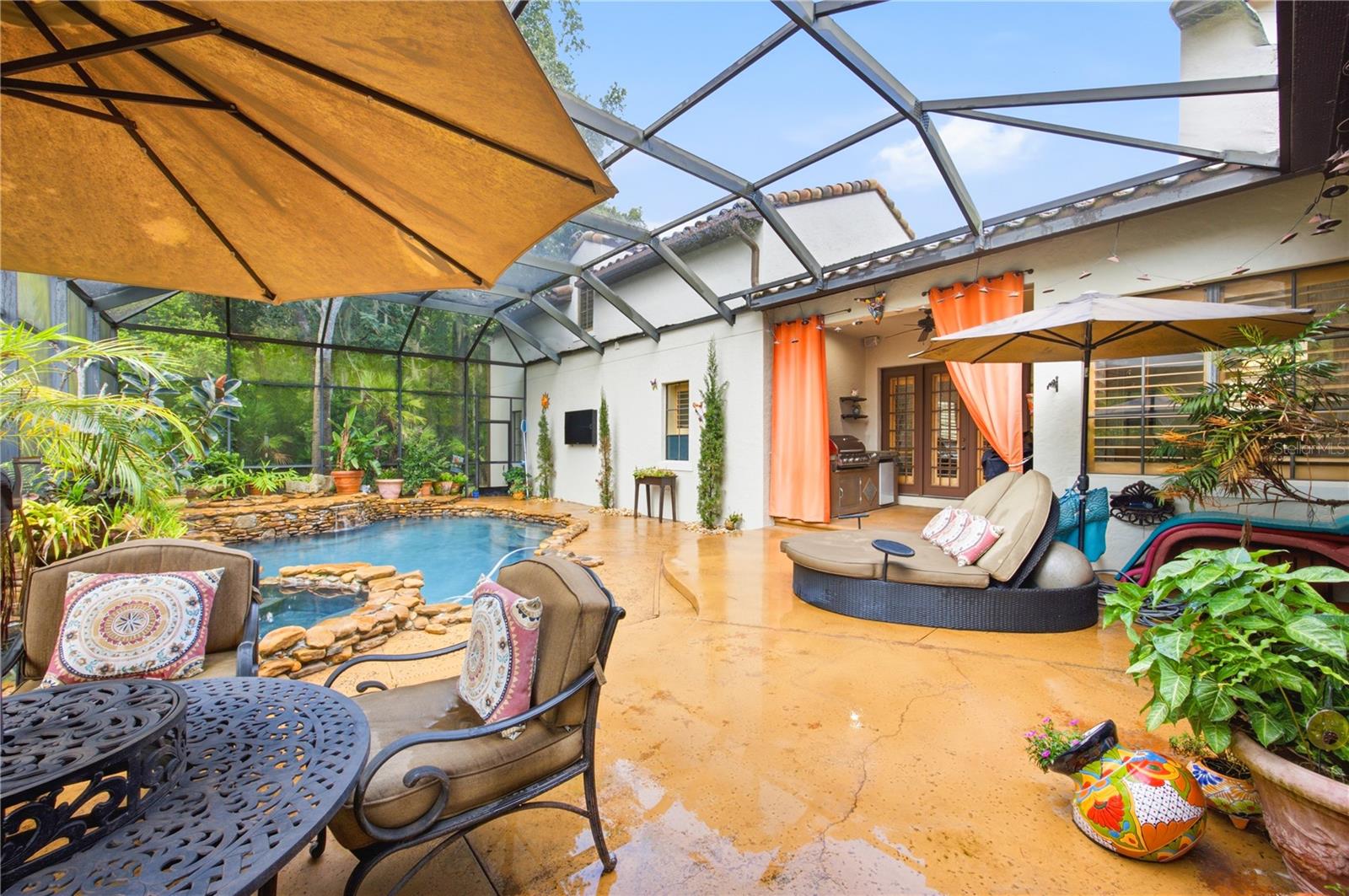 Screened pool patio with a stone-edged pool, tropical plants, and orange curtains.