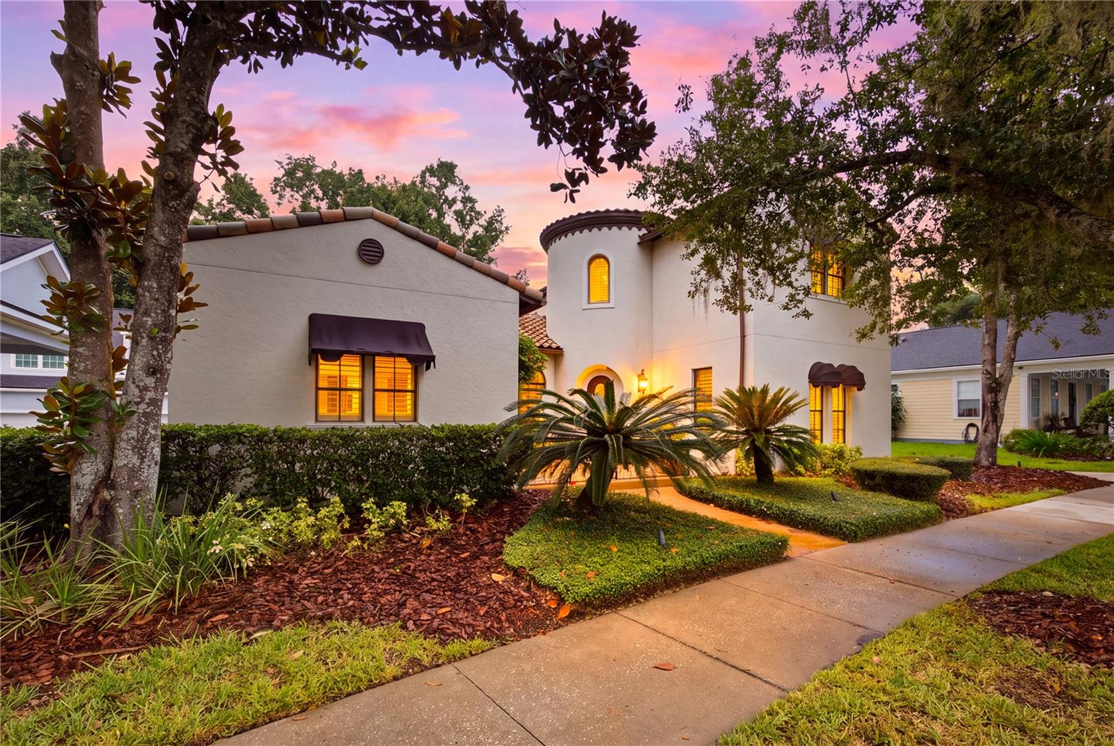 White stucco home with a rounded tower and palm landscaping, photographed at dusk.