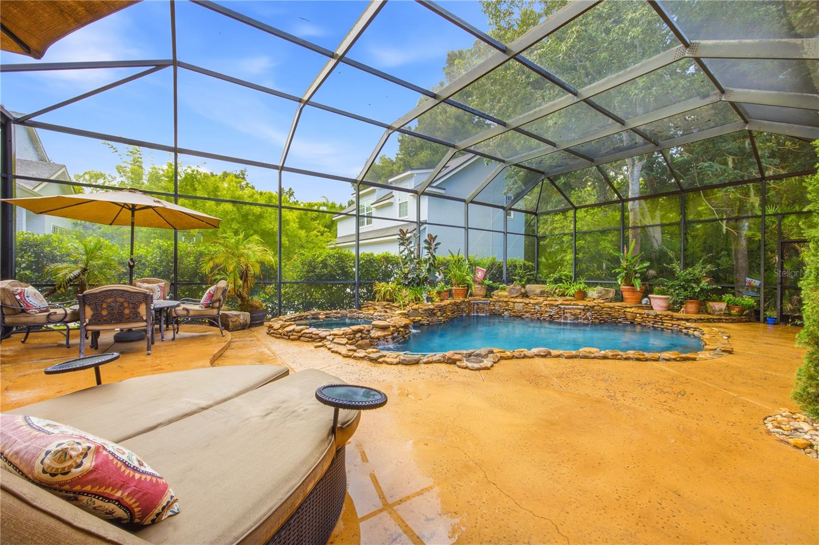 Screened pool patio with a stone-edged pool, lounge chairs, and potted plants.