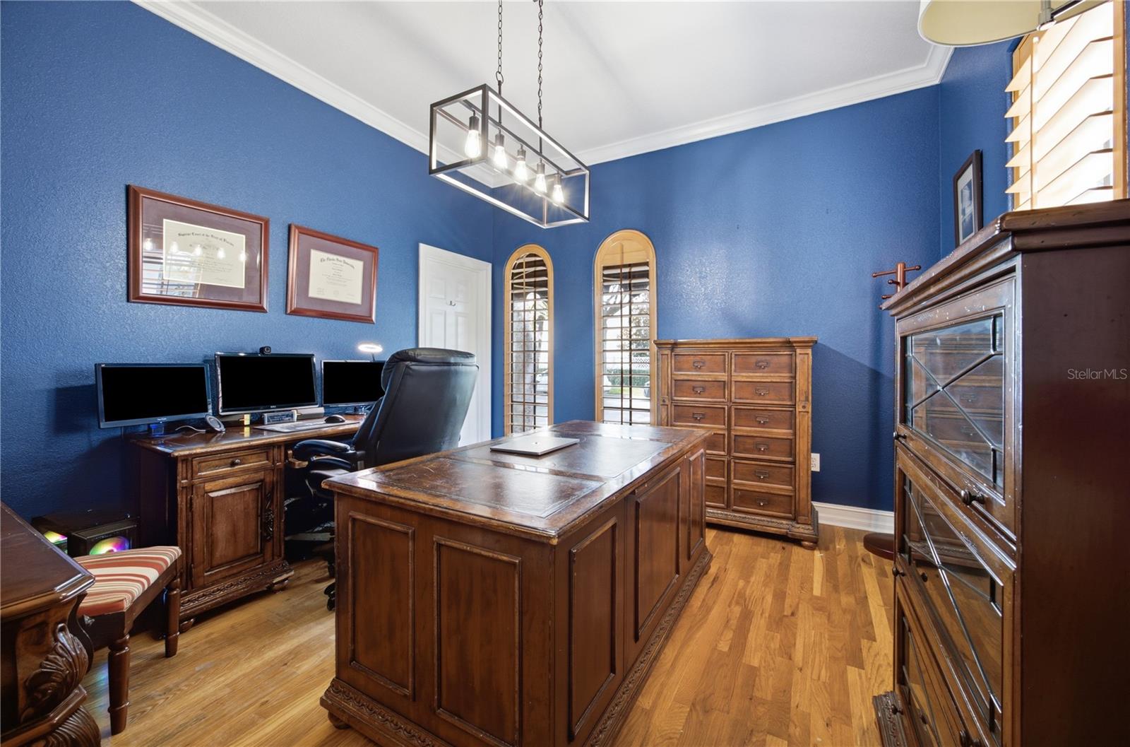 Blue-walled home office with a large wooden desk, matching cabinets, and hardwood floors.