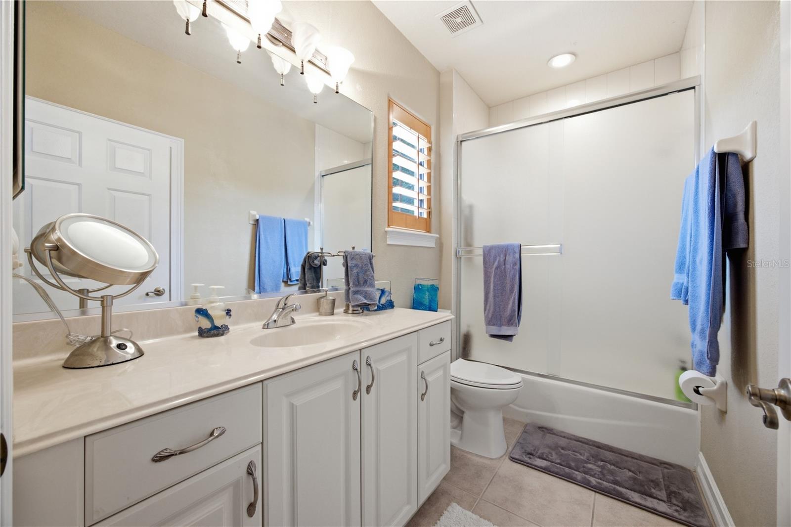 Bathroom with a long white vanity, large mirror, and bathtub-shower enclosure.