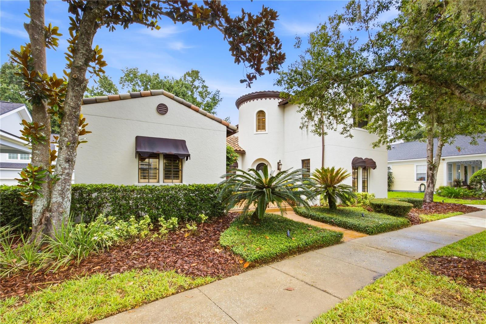 White stucco home with a round tower, terracotta roof tiles, and landscaped front garden.