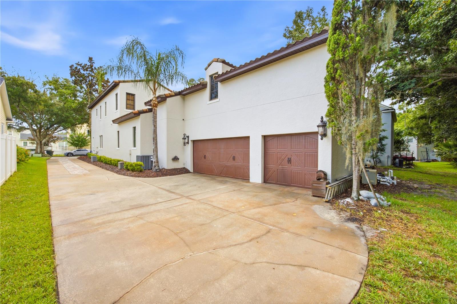White stucco two-story home with tile roof, brown garage doors, and broad curved driveway.