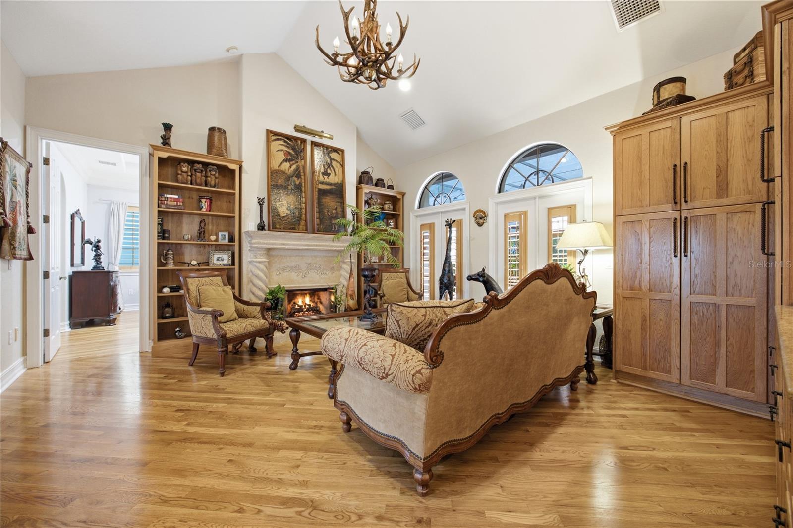 Living room with a carved fireplace, vaulted ceiling, and arched windows.
