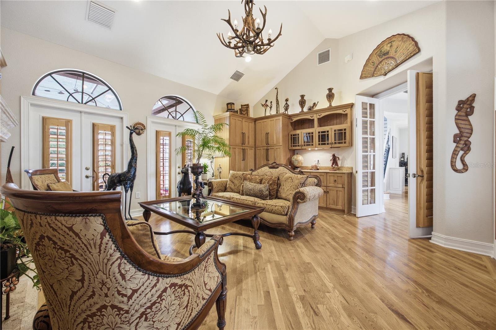 Living room with patterned seating, arched shuttered windows, hardwood floors, and built-in wood cabinetry.
