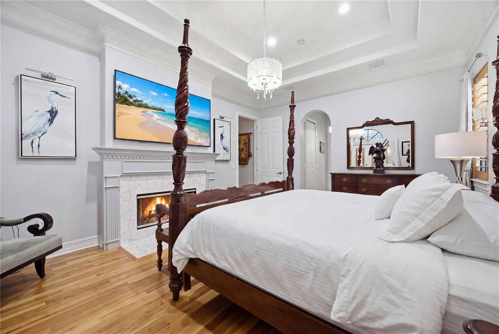 Bedroom with a four-poster bed, lit fireplace, hardwood floors, and crystal chandelier.